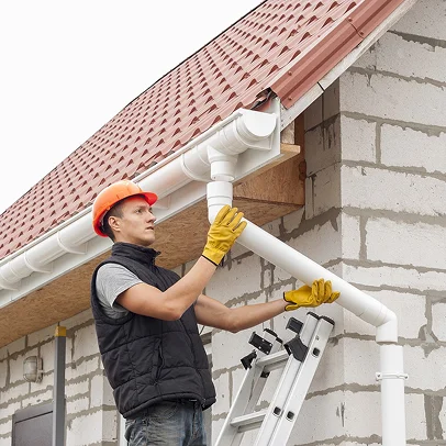Homme avec casque de sécurité installant des gouttières blanches sur une maison en construction à Sartrouville dans les Yvelines 78