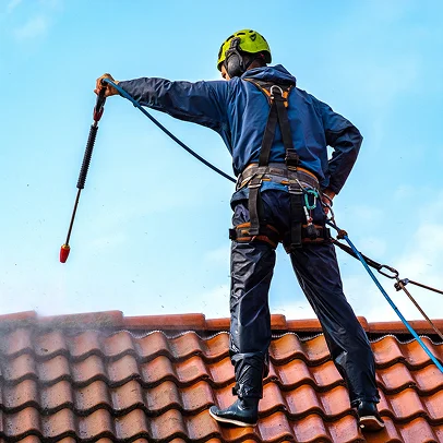 Homme en harnais, nettoie un toit de tuiles avec un nettoyeur haute pression à Sartrouville dans les Yvelines 78