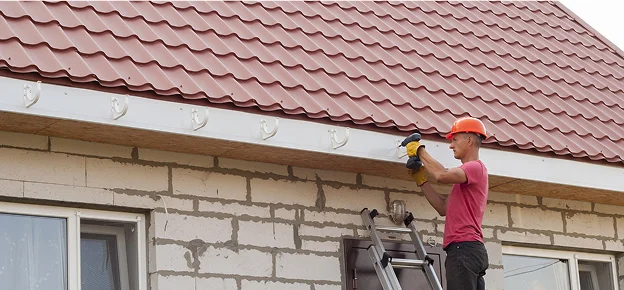 Un homme installe une gouttière blanche sur une maison au toit rouge à Sartrouville dans les Yvelines 78