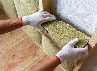 Mains gantées installant de l'isolation en laine minérale dans une structure murale en bois à Sartrouville dans les Yvelines 78